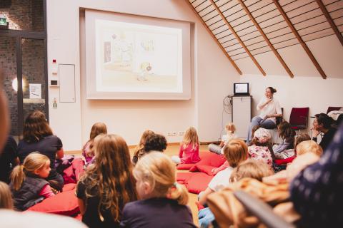 Mehrere Kinder sitzen auf Kissen und sehen sich ein Bilderbuchkino an.