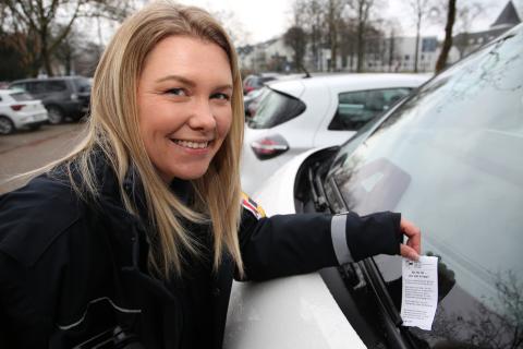 Eine Frau heftet ein Knöllchen an eine Auto.