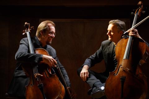 2 Männer, welche vor einem schwarzen Hintergrund Cello spielen.