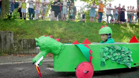 Ein Kind in einer grünen Seifenkiste im Drachendesign.