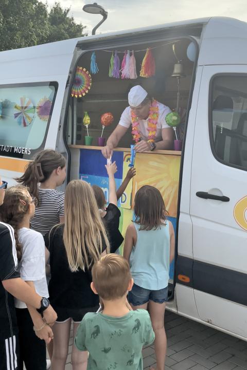 Der Bürgermeister teilt Eis an Kinder aus.